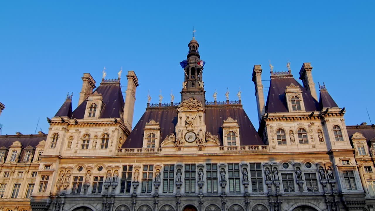Ornate historic Parisian building with a central clock tower and steep slate rooftops under a clear blue sky