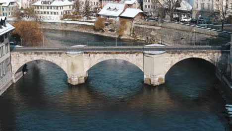 coche pasando por un viejo puente de piedra mientras el agua fluye durante el invierno en berna, suiza