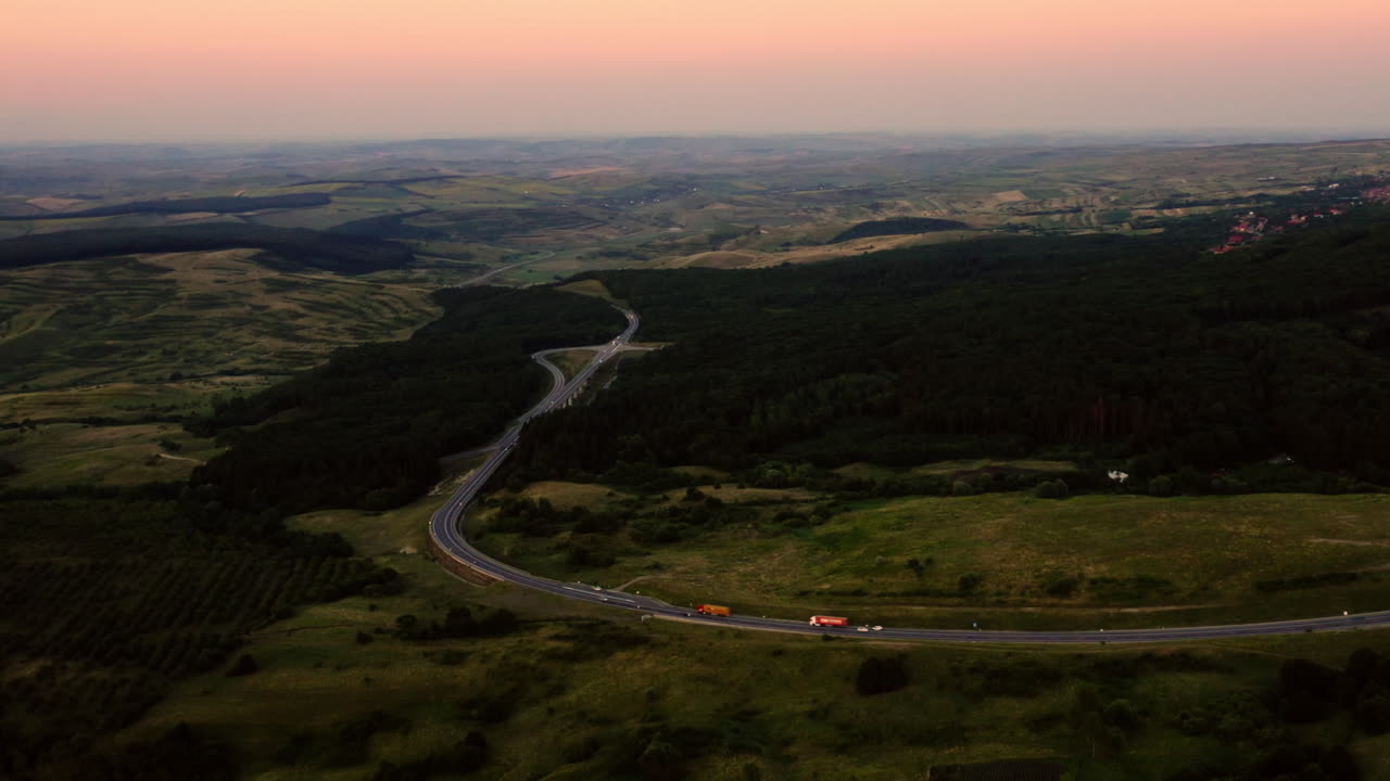 vista aérea del paisaje de drones sobre una carretera que serpentea a través de un bosque y un campo rumanos, al atardecer