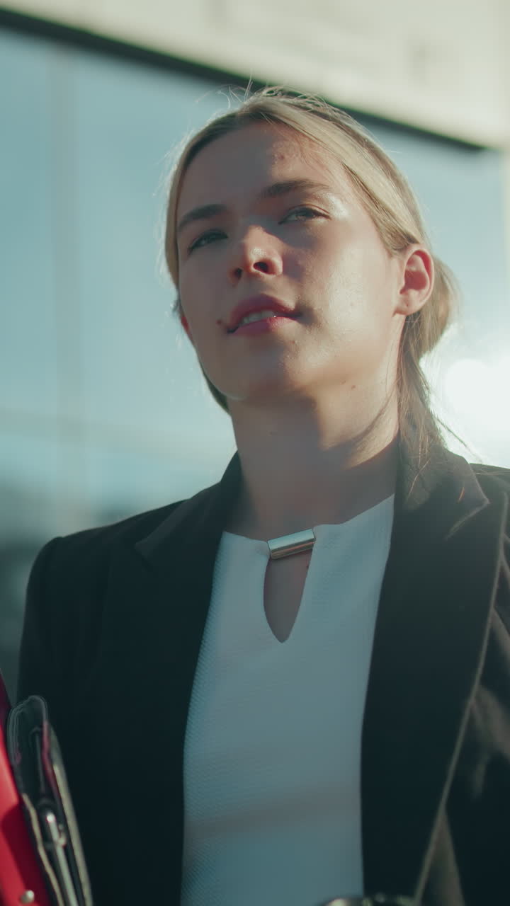 Business lady on break holding form and fruit juice walking confidently with sunlight ambiance reflecting off modern building, creating dynamic urban vibe of professionalism
