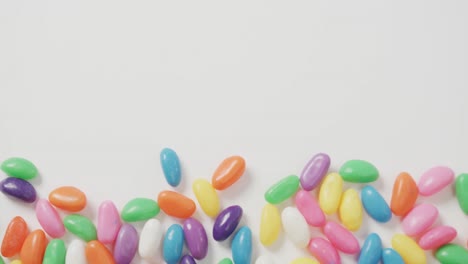 video of overhead view of multi coloured sweets with copy space over white background