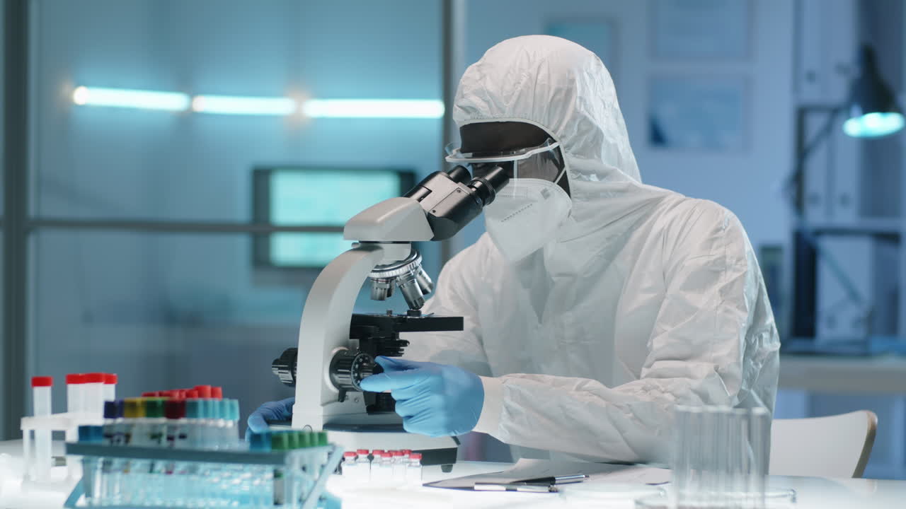 Black Doctor in Protective Suit Working with Microscope in Lab
