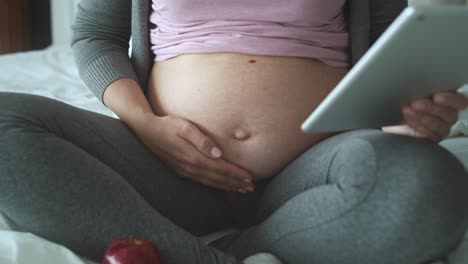 tracking left video of unrecognizable pregnant woman using tablet in bed.