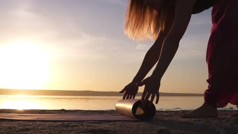 Nahaufnahme-Einer-Yogi-Frau,-Die-Eine-Yogamatte-Auf-Einem-Sand-In-Der-Nähe-Des-Wassers-Ausbreitet.-Sonne-Scheint.-Morgendämmerung