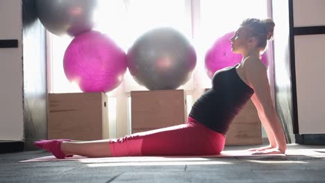 pregnant woman strokes belly while sitting on yoga mat happy pregnant woman sits on yoga mat and gently strokes belly in front of window future mom prepares to exercise and relax during yoga
