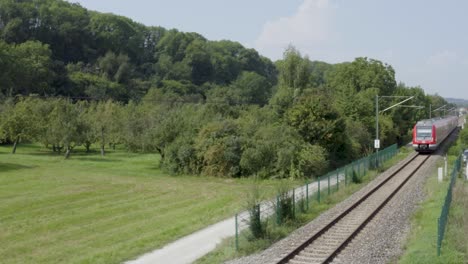 Red-train-traveling-through-lush-green-countryside-in-daylight