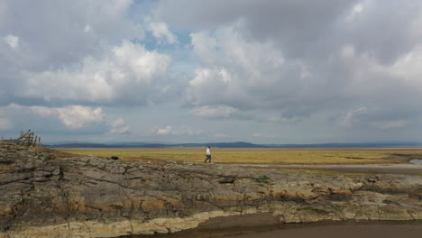 toma aérea amplia de una persona caminando por las rocas en la costa durante la marea baja, en los brillantes días de verano