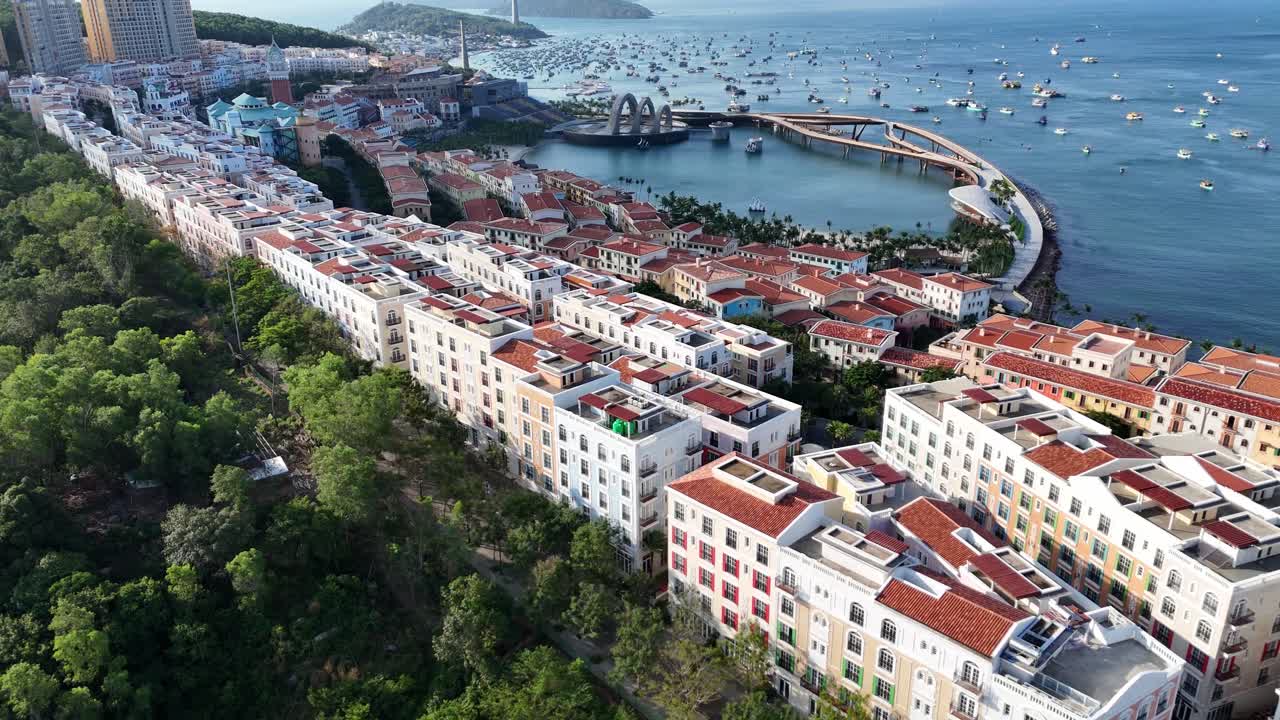 Aerial footage of Phu Quoc Island, Vietnam. coastal region, featuring high-rise buildings, residential complexes. There is a clear view of the coastline, with boats scattered in the water
