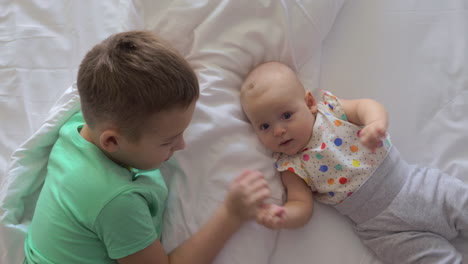 boy and baby girl siblings on bed at home