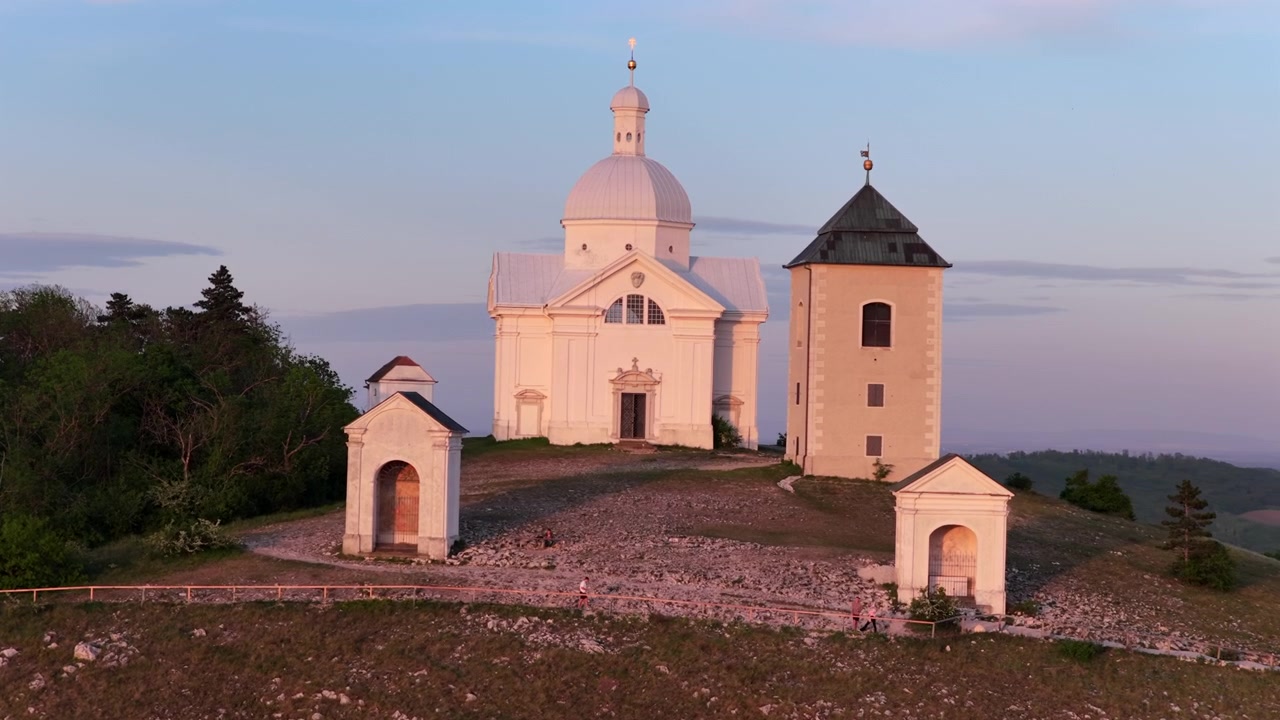 Letecký pohled z dronu na poutní cestu Křížové cesty a bílou barokní kapli na Svatém Kopečku (Svaty Kopecek) za soumraku s jemnou růžovou oblohou, Mikulov, Jižní Morava, Česká republika.