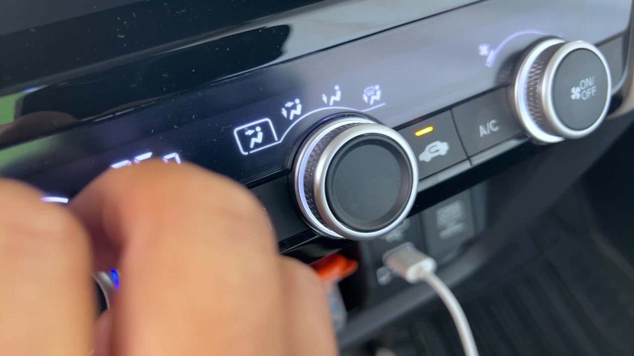 Primo piano di una mano che regola la manopola del controllo climatico sul cruscotto di un veicolo, modificando le impostazioni del flusso d'aria sul pannello di controllo dell'aria condizionata dell'auto.