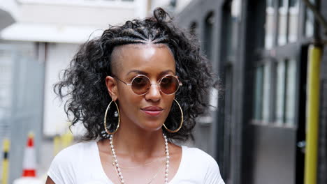 joven negra de moda girando y mirando a la cámara sobre sus gafas de sol redondas, y riendo, de cerca