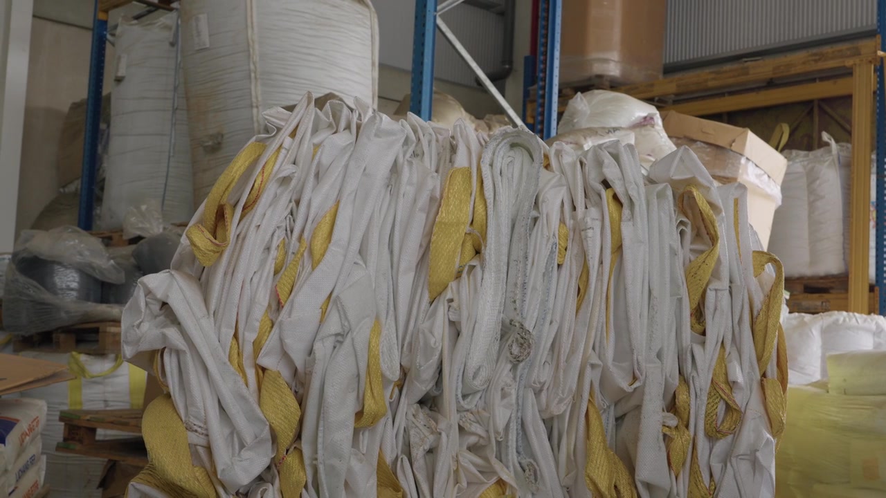 Grande fascio di cinghie di plastica bianche e gialle ammucchiate sul pavimento all'interno di un impianto di magazzino industriale.