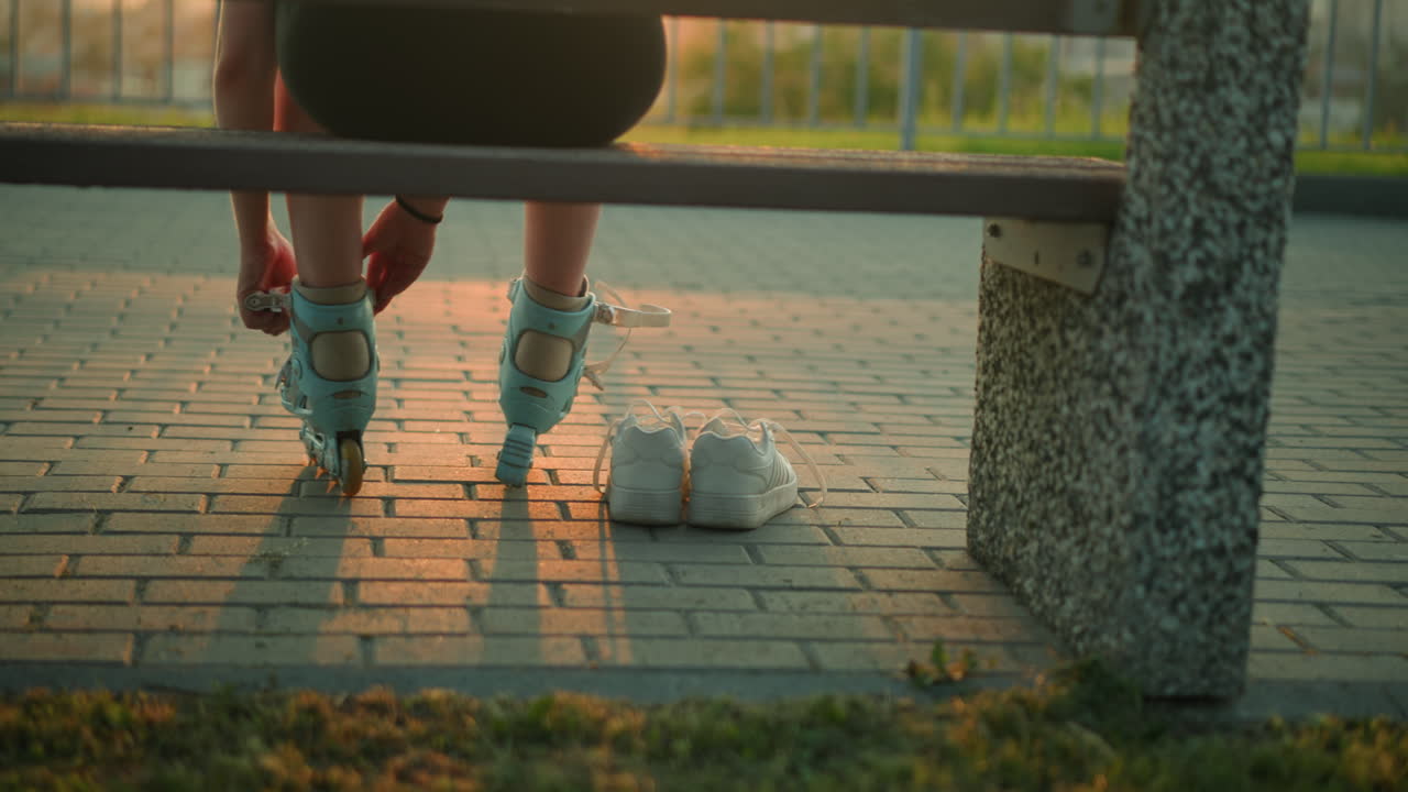 저녁 빛에 벤치에 앉아있는 젊은 여자의 뒷면, 바닥에 그녀의 에 두 개의  스니커와 함께 롤러 스케이트의 줄을 제거