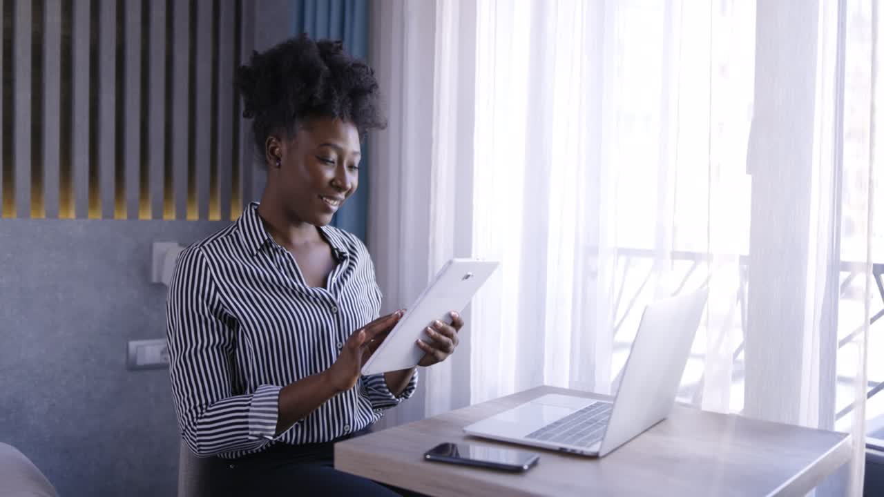 A happy young black woman who relaxes on a chair in a hotel room