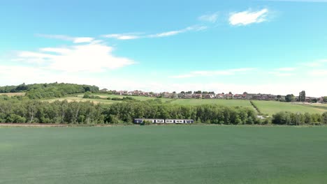 Train-moving-between-green-meadows-near-Wombwell-town,-England,-sunny-day