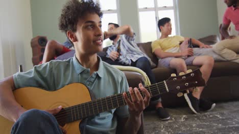 Felices-Amigos-Varones-Diversos-Tocando-La-Guitarra-Y-Hablando-En-La-Sala-De-Estar