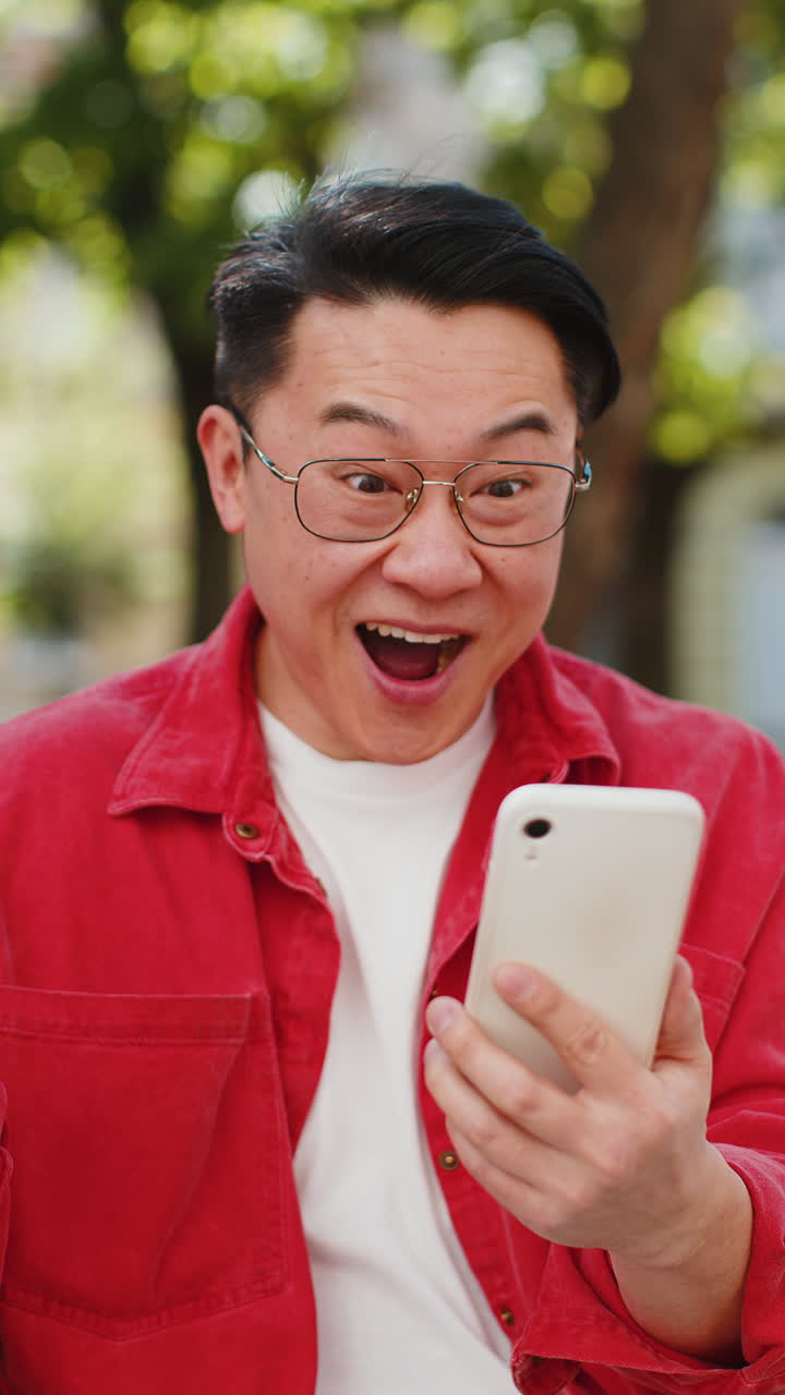 Uomo asiatico maturo felice e eccitato usa lo smartphone per festeggiare la vittoria Buone notizie per strada in città