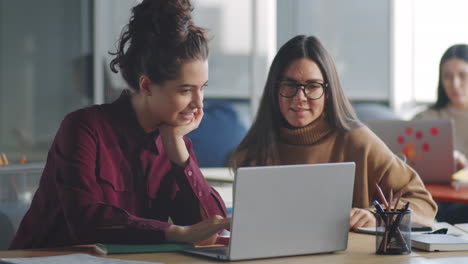 Dos-Colegas-Mujeres-Que-Usan-Una-Computadora-Portátil-Y-Hablan-En-El-Trabajo