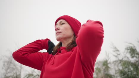 close-up of coach with hands on shoulders wearing gloves and beanie, turning arm with focused expression, snow-covered background featuring frosted trees