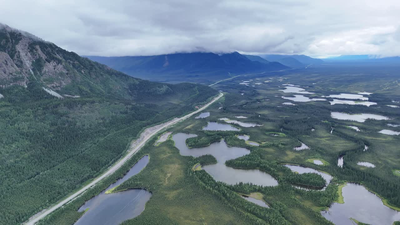Dramatic Alaska mountain range covered in mist with lush green forest and a scenic highway winding through stunning landscape for travel adventure concept