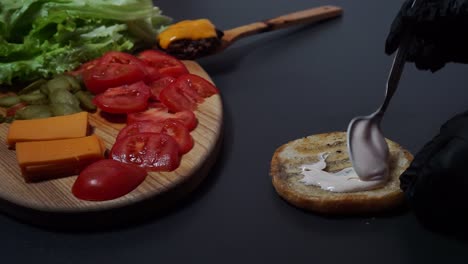 Static-above-closeup:-Spreading-sauce-on-burger-bun-aside-delicious-salad-board