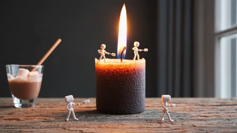 Tiny figurines roasting marshmallows over flickering candle flame, accompanied by hot chocolate glass nestled on wooden surface, creating whimsical miniature scene of cozy comfort