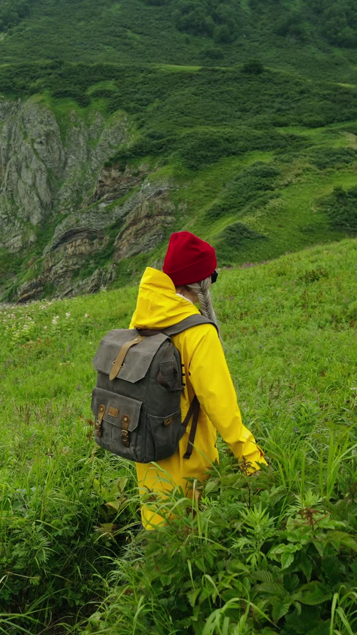 Donna in impermeabile giallo che fa escursioni attraverso un paesaggio montano verde