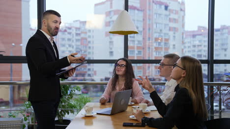 man in suit discussing work moments with colleagues sitting at the table in front of him. working team having conversation at the cup of coffee in office.