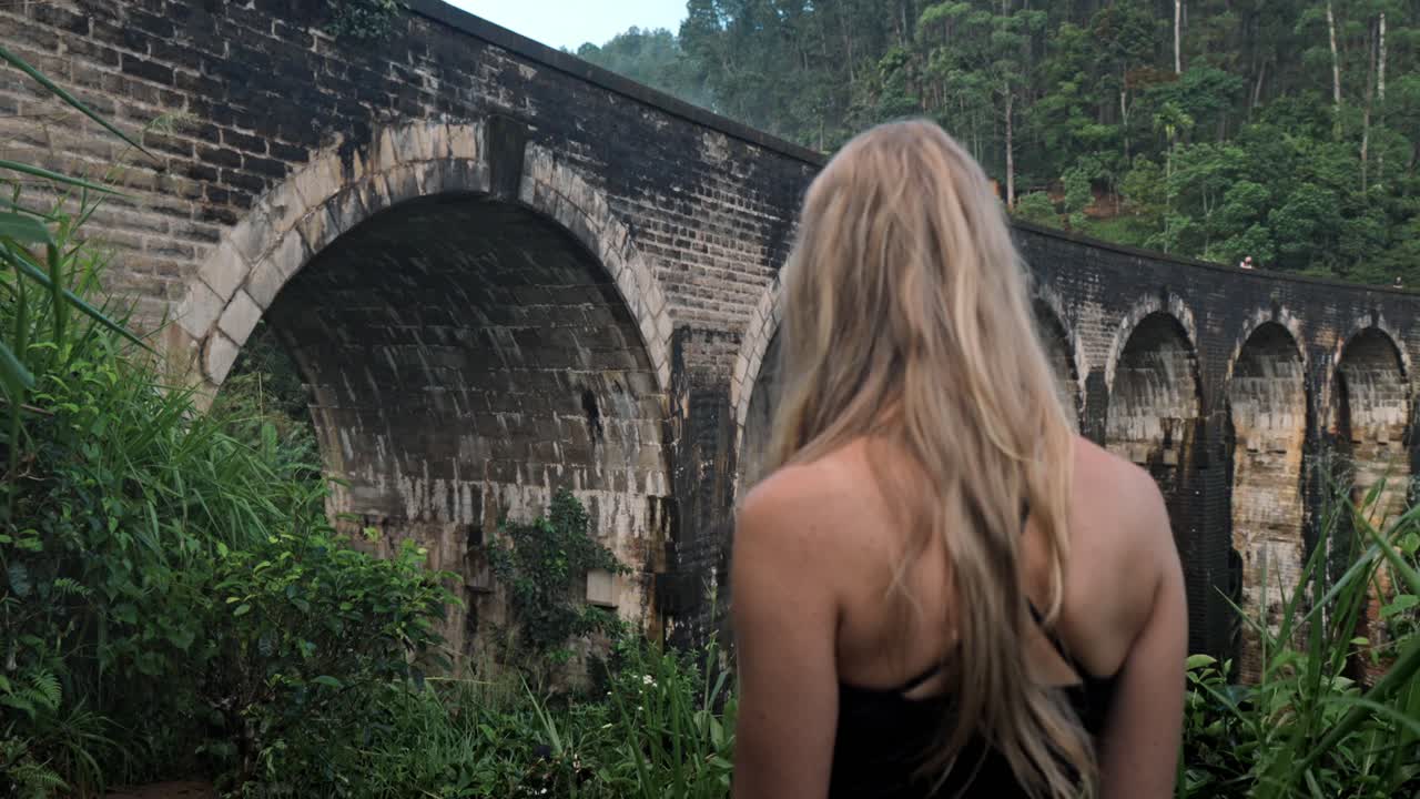 A young woman observes the historic Nine Arch Bridge from a nearby hillside in Ella, Sri Lanka.