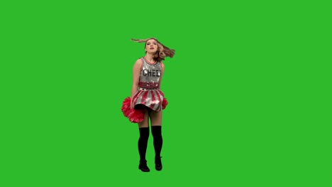 una adorable animadora en uniforme con pom-poms rojos realiza un baile jubiloso. retrato de una joven mujer sonriente bailando en el estudio en una pantalla verde. cámara lenta