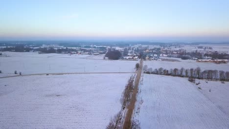 Birds-eye-view-of-winter-landscape-showing-snow-blanket-over-rural-village-and-countryside-fields