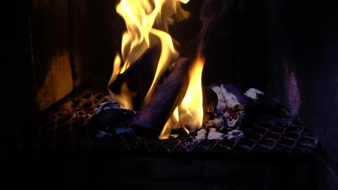 Slow motion panning shot of fire burning up in flames from small wood log and coal. close up view of a cooking tandoor grill from kitchen