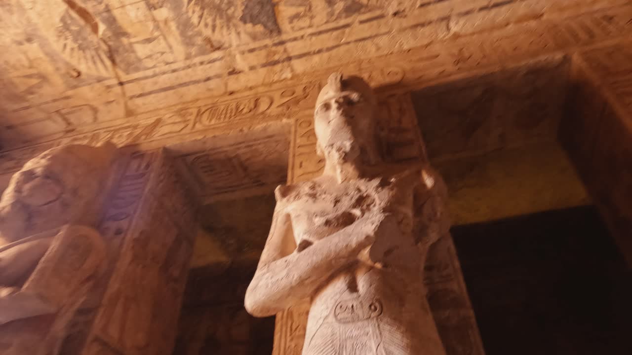 Dramatic interior view of the Abu Simbel Temple in Egypt, highlighting monumental statues of Pharaoh Ramses II and intricate hieroglyphics on the walls and ceiling.