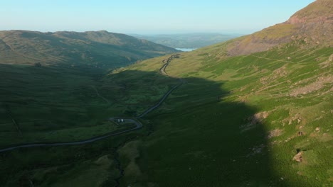 shadowed mountain pass road at sunrise with parked camper vans in valley. summer. kirkstone pass, lake district, cumbria, uk