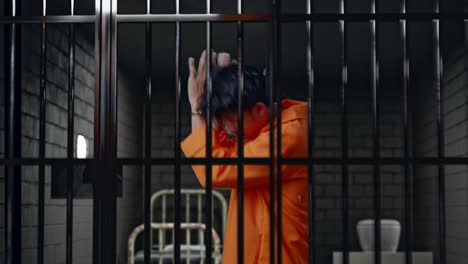 vista lateral de un prisionero masculino asiático con esposas de pie en la cárcel, mostrando el signo de la palma de la mano la expresión de no ser querido para ser capturado por la cámara