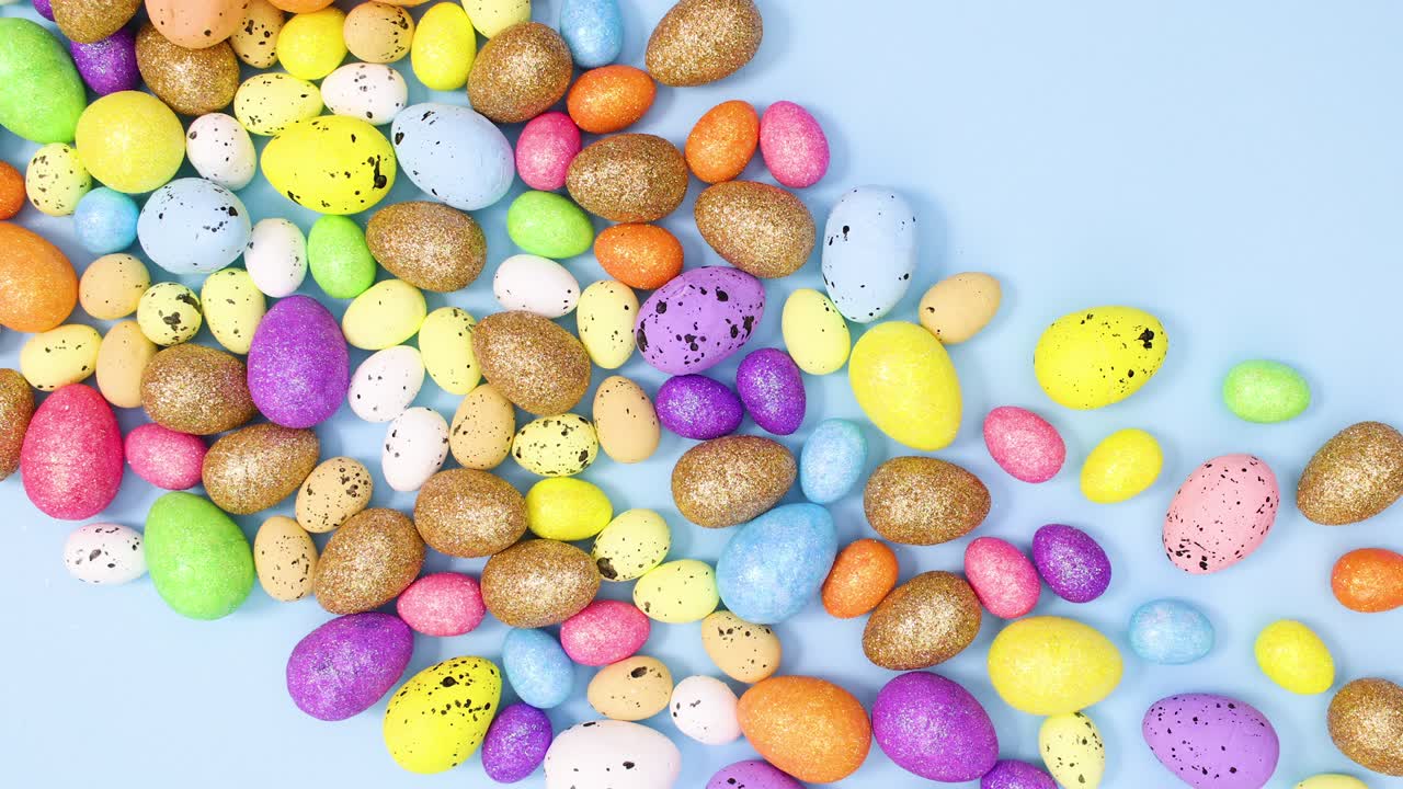 Spilled vibrant Easter eggs on pastel blue background. Stop motion flat lay