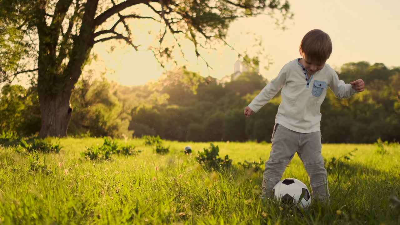 en cámara lenta el niño juega graciosamente con una pelota de fútbol en un prado al atardecer