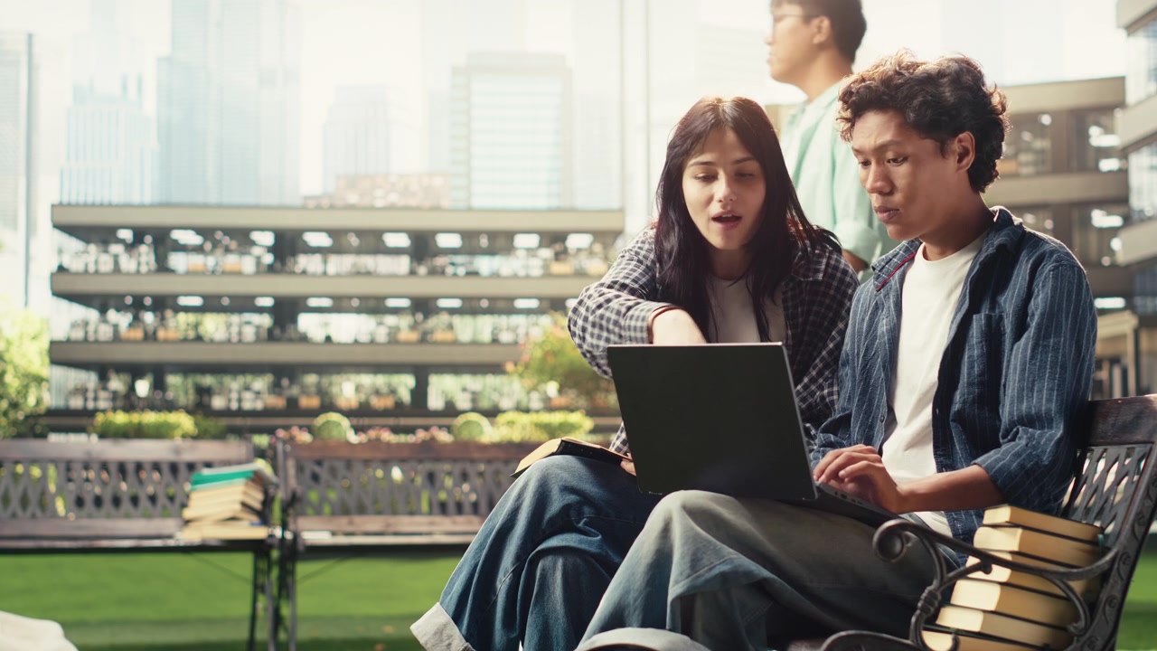 Diverse classmates collaborating on laptop while seated on campus bench