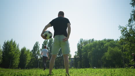 back view of a man rotating a soccer ball around him while his son kicks a ball and an elderly man chases after it