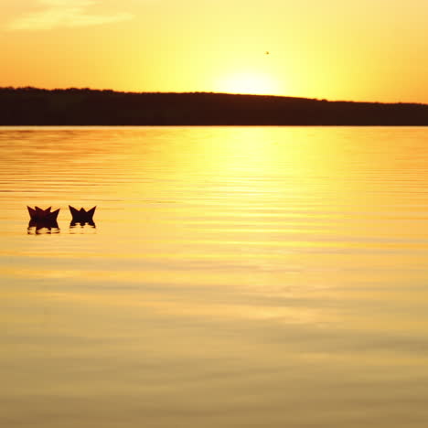 good sunset with the reflection in the water and many paper boats floating in the river. origami ships on water in the evening