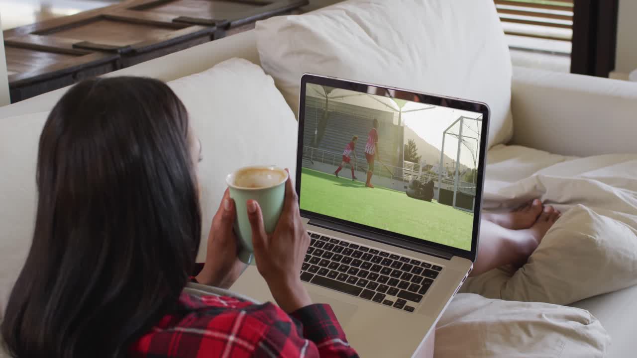 Composite of woman sitting at home holding coffee watching hockey match on laptop