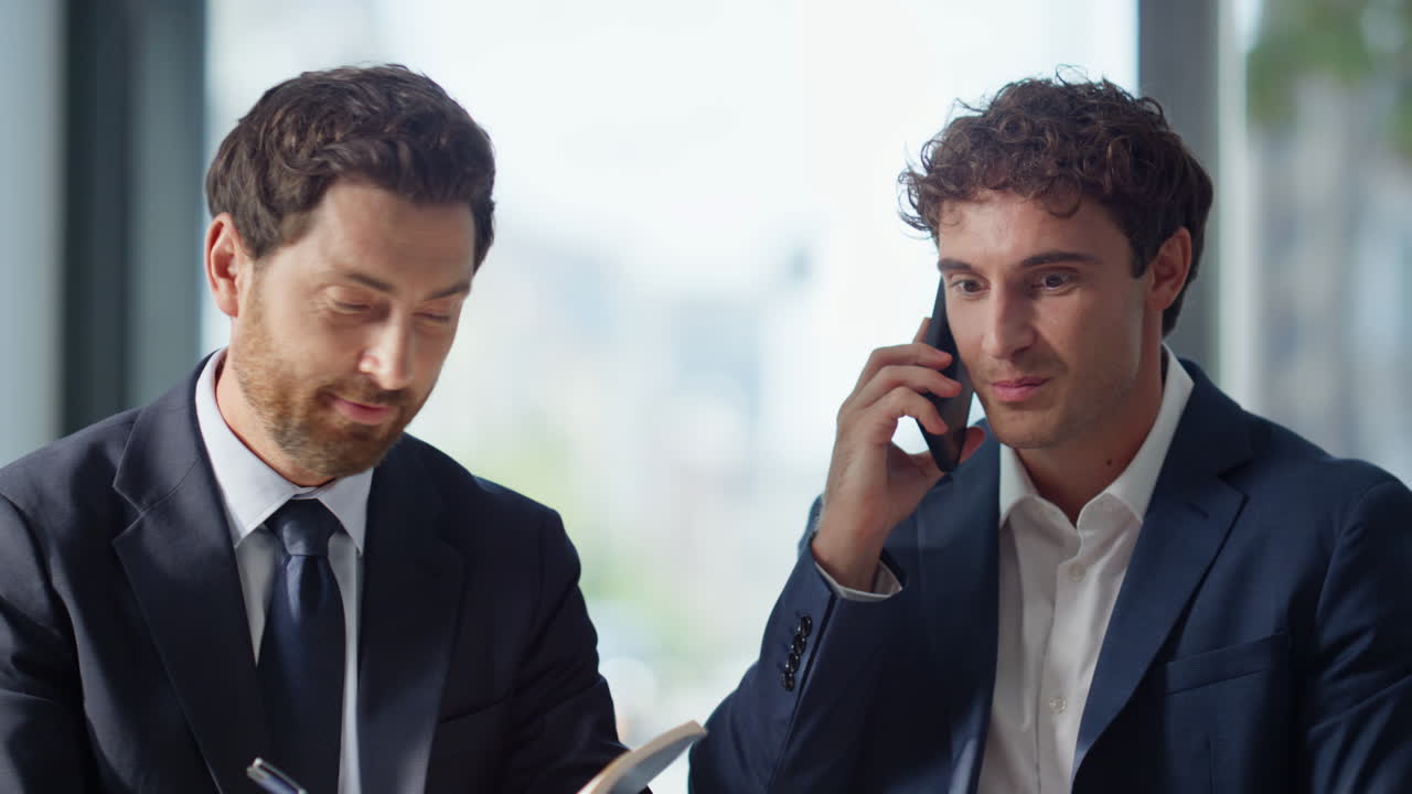 Dirigente entusiasta che parla al cellulare in ufficio panoramico. Uomini d'affari esultanti