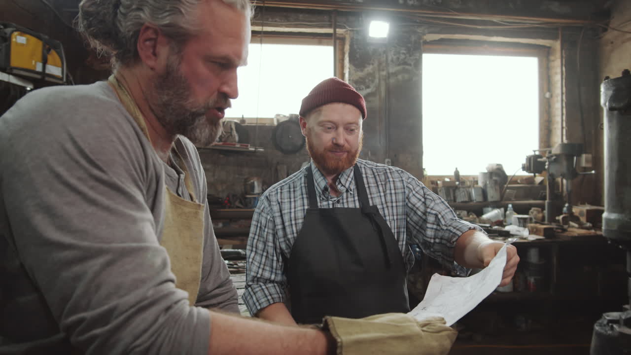 Two Blacksmiths Discussing Paper in Workshop