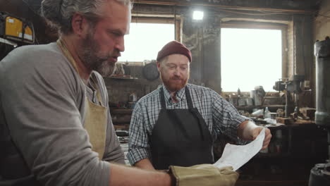 two blacksmiths discussing paper in workshop