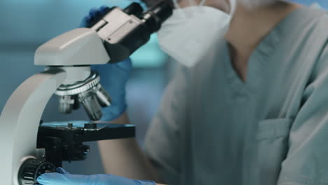 científica de laboratorio en uniforme de protección usando el microscopio