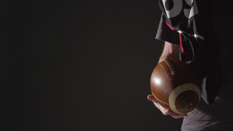 close up studio shot of american football player holding ball with low key lighting