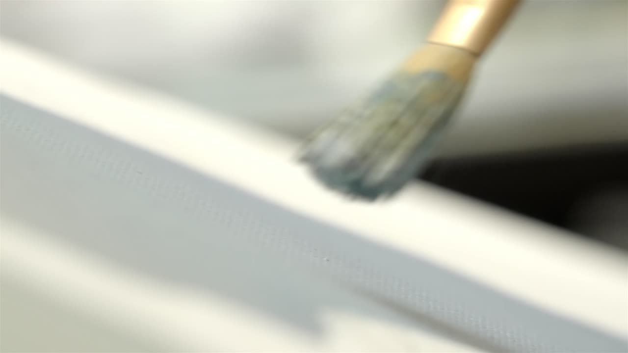 Close up of paint brush applying blue oil paint on white canvas
