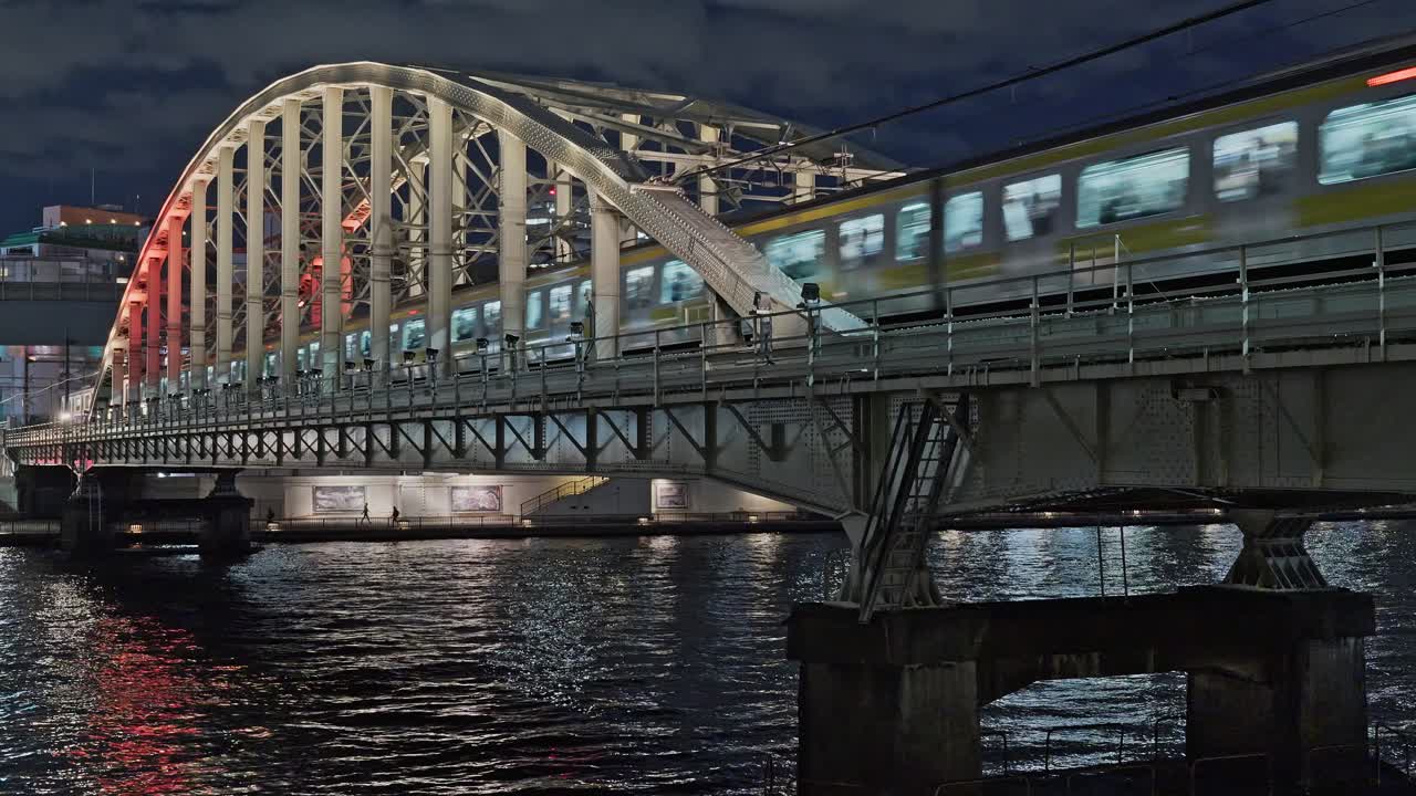 Et oplyst, gult tog krydser den historiske jernbanebro i stål over Sumida-floden