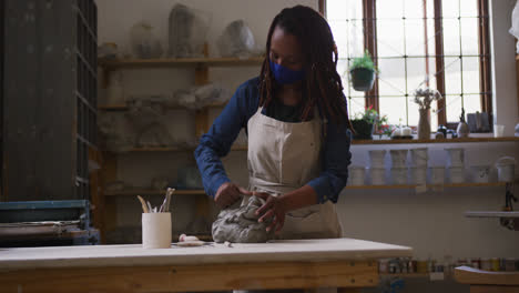 female potter wearing face mask and apron kneading the clay at pottery studio